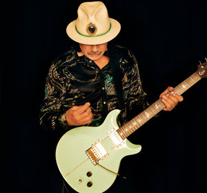 Santana playing a light green electric guitar against a black background